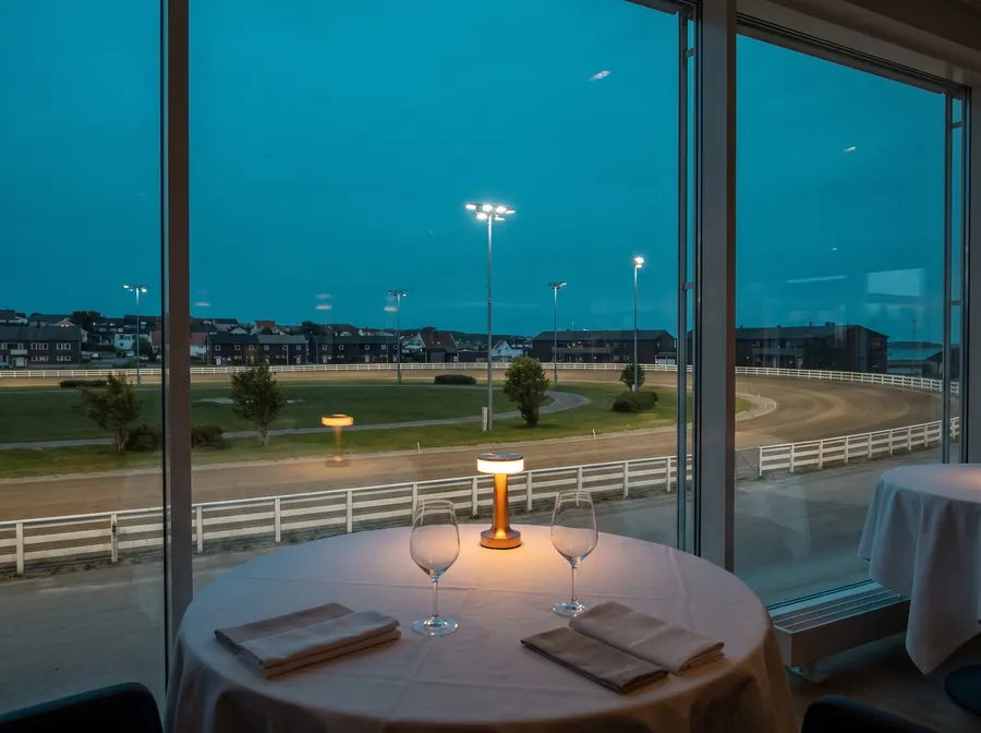 Generated scene: a table for two by a tall window at blue hour, with a floodlit dirt racing oval beyond; not a photograph of the restaurant.
